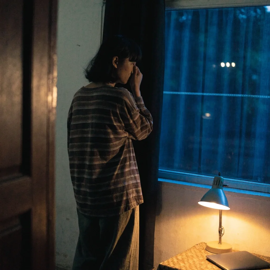 A person closing a laptop and turning to look toward a window in evening light