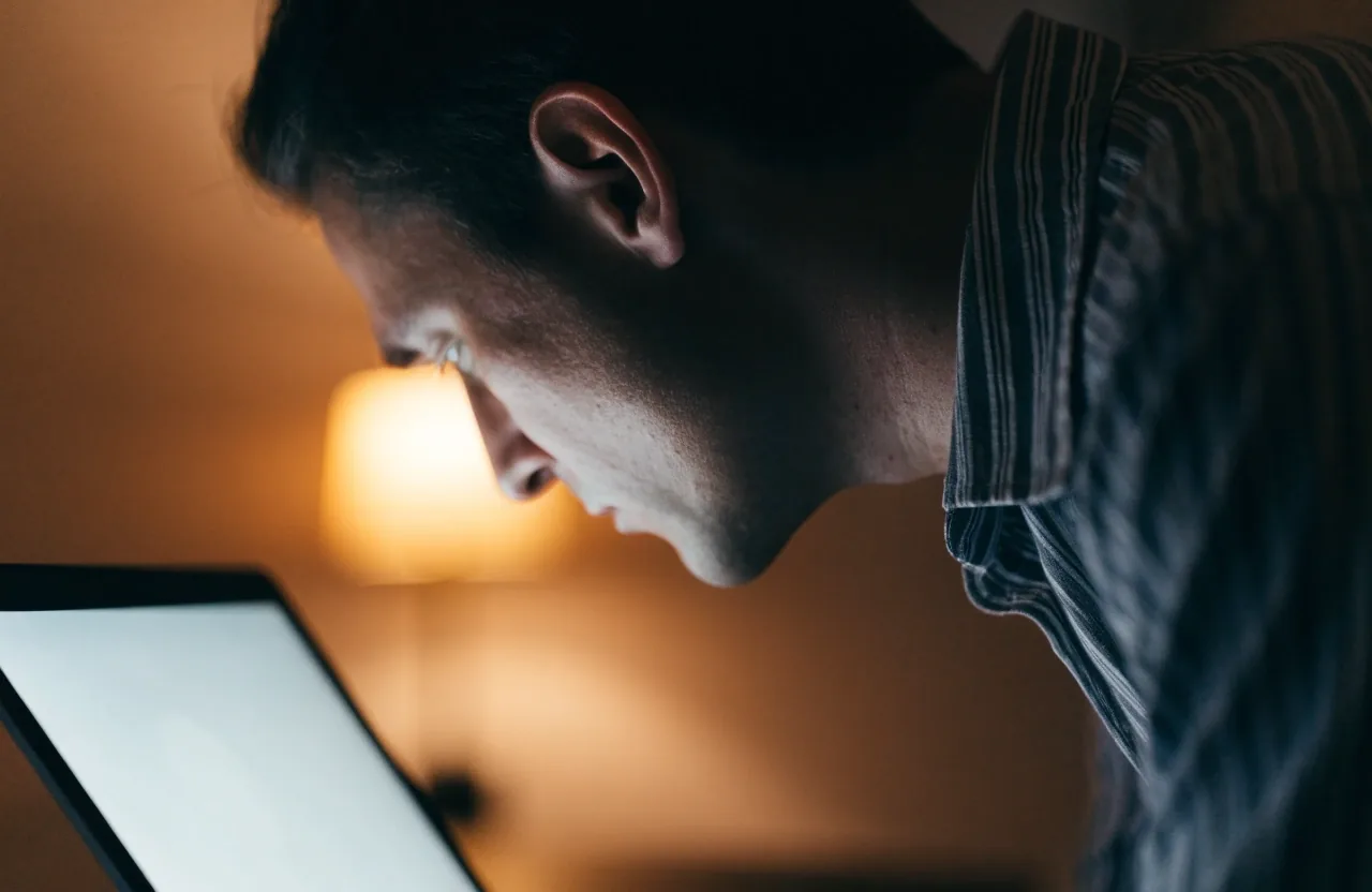 Side view of a person tipping the head forward toward a bright laptop screen